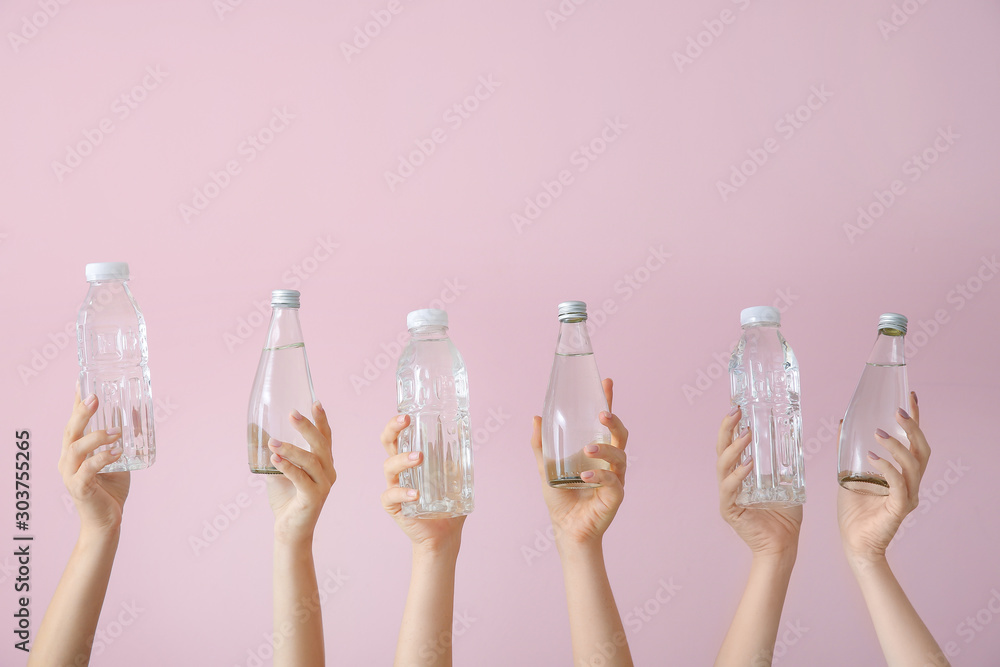 Female hands with bottles of water on color background