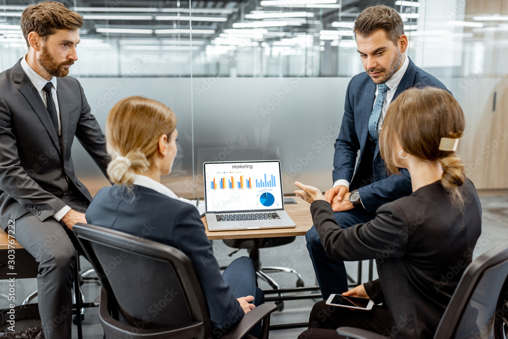 Group of strictly dressed business people discussing financial graph presented on the laptop, meetin