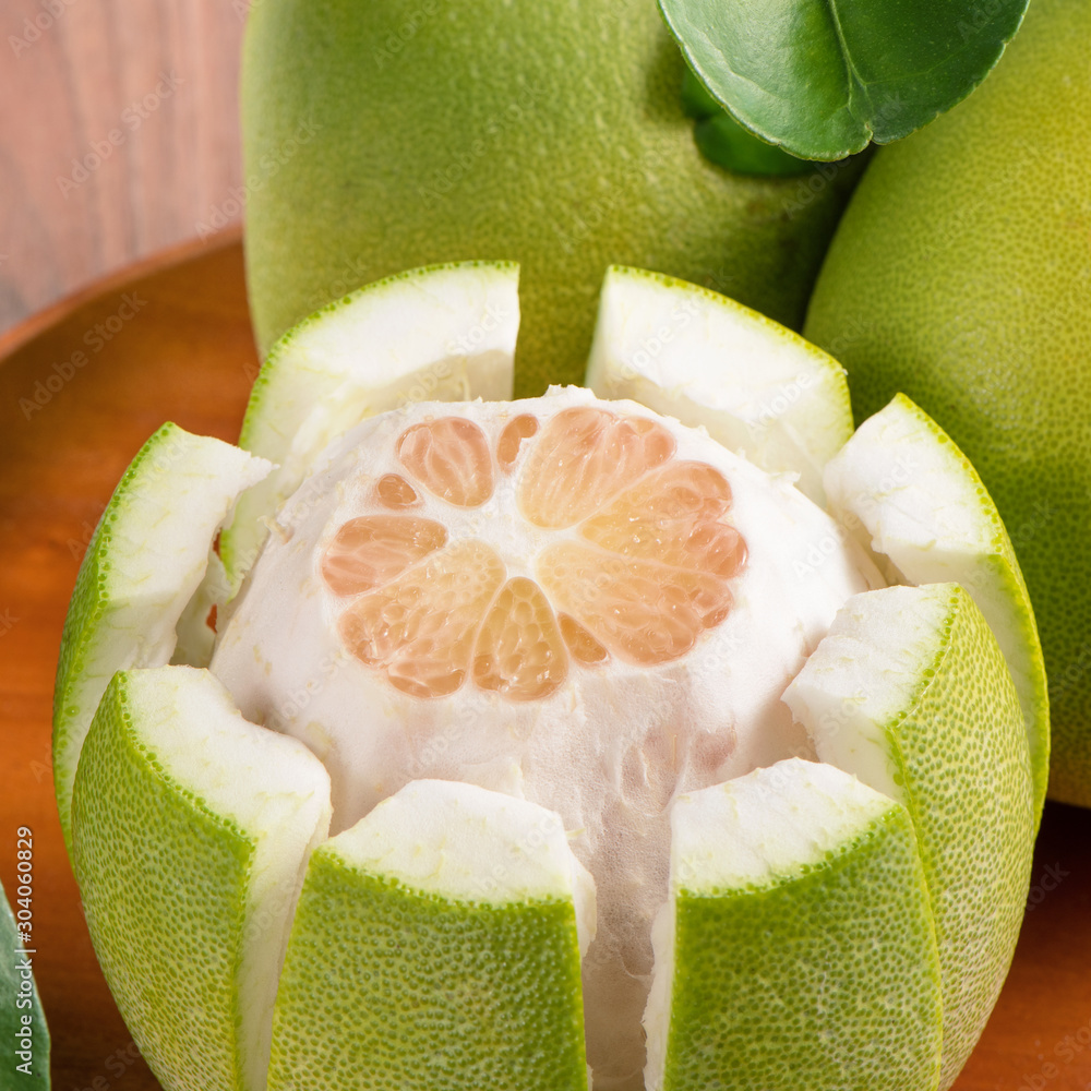 Fresh peeled pomelo, grapefruit, shaddock with green leaves on dark wooden plank table. Seasonal fru