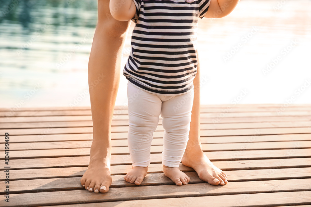 Mother teaching her little baby to walk near river