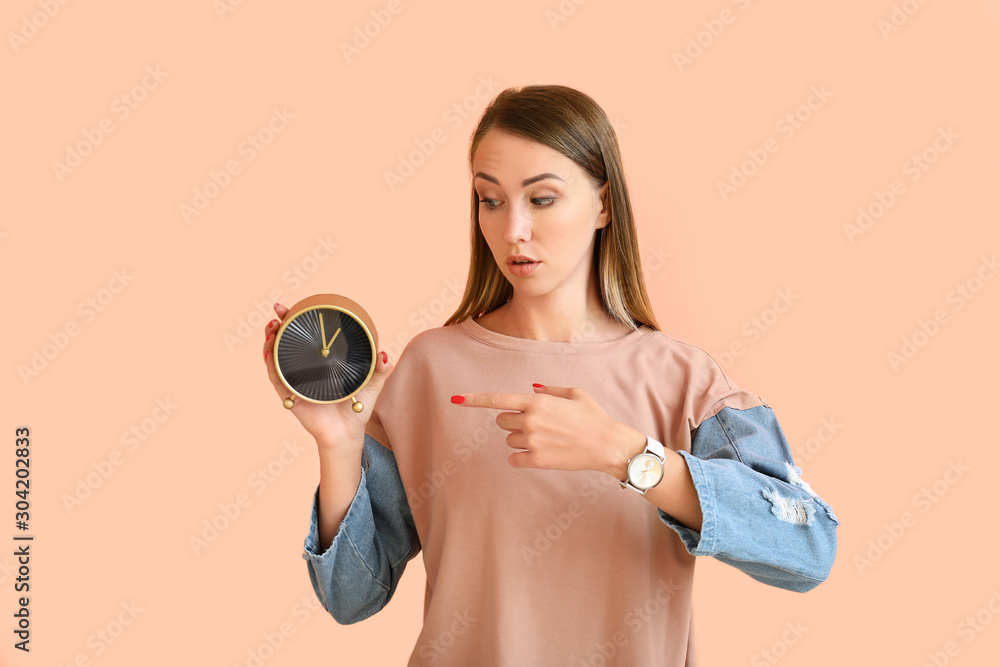 Beautiful young woman with alarm clock on color background