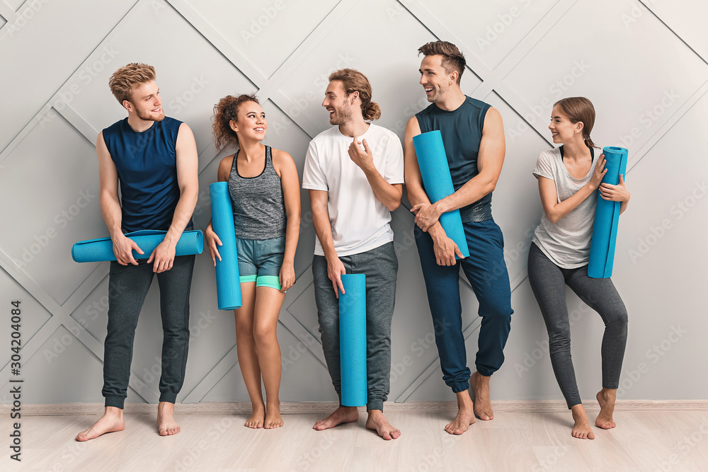 Group of people with yoga mats near light wall