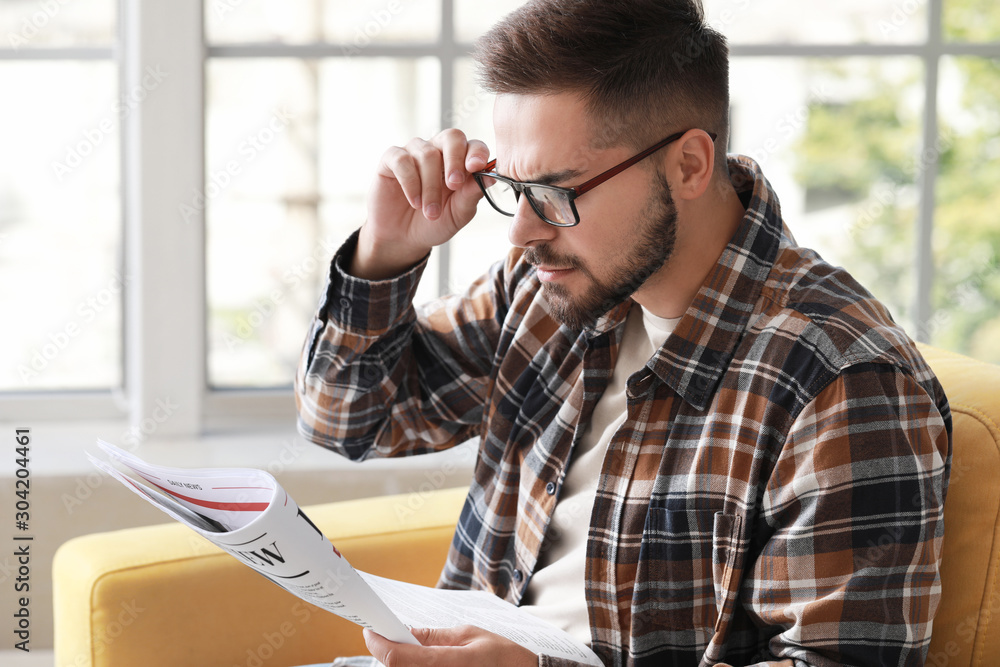 Worried man reading newspaper at home