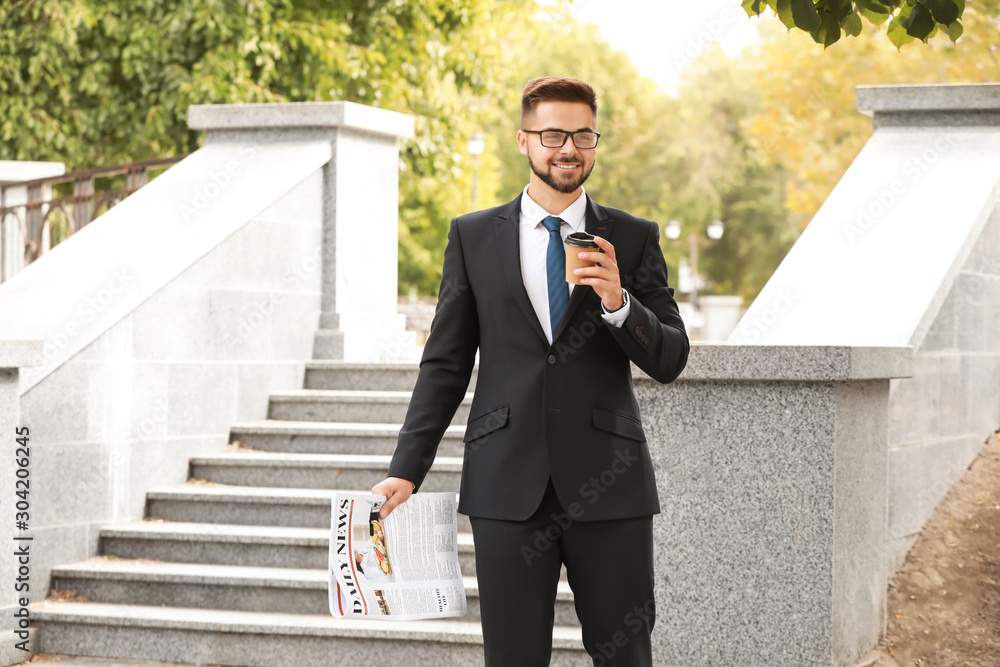 Handsome businessman with newspaper and coffee outdoors