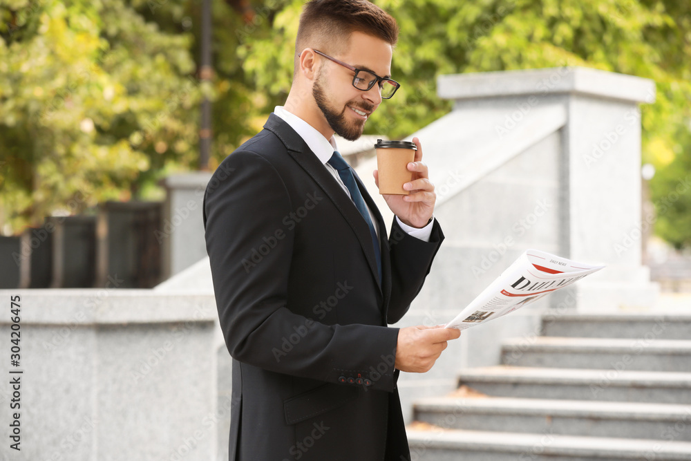 Handsome businessman with newspaper and coffee outdoors