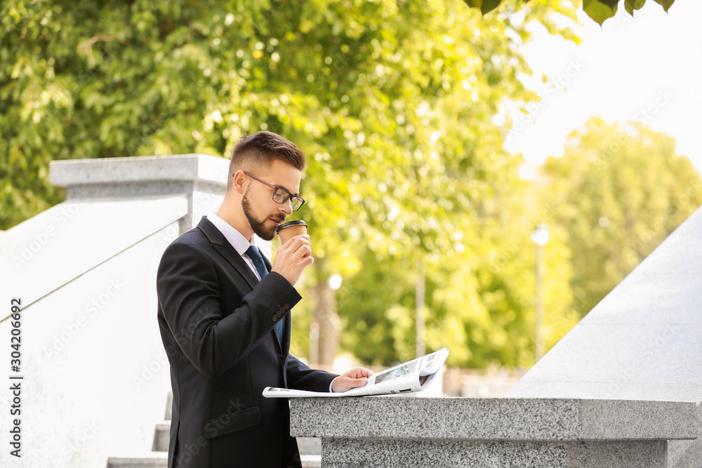 Handsome businessman with newspaper and coffee outdoors