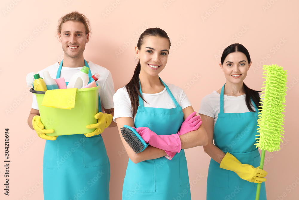 Team of janitors with cleaning supplies on color background