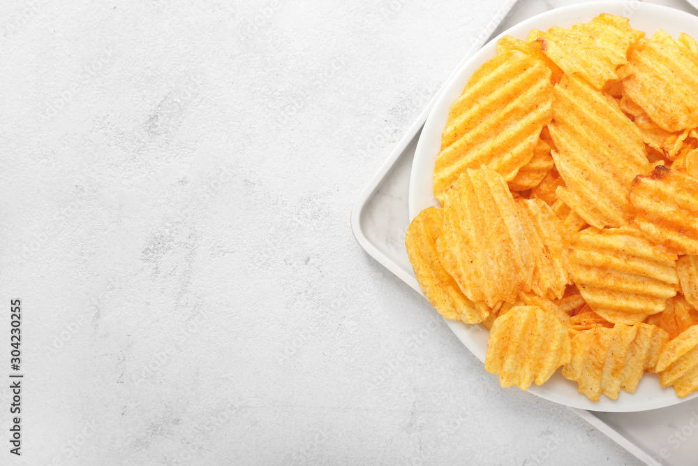 Plate with tasty potato chips on light background