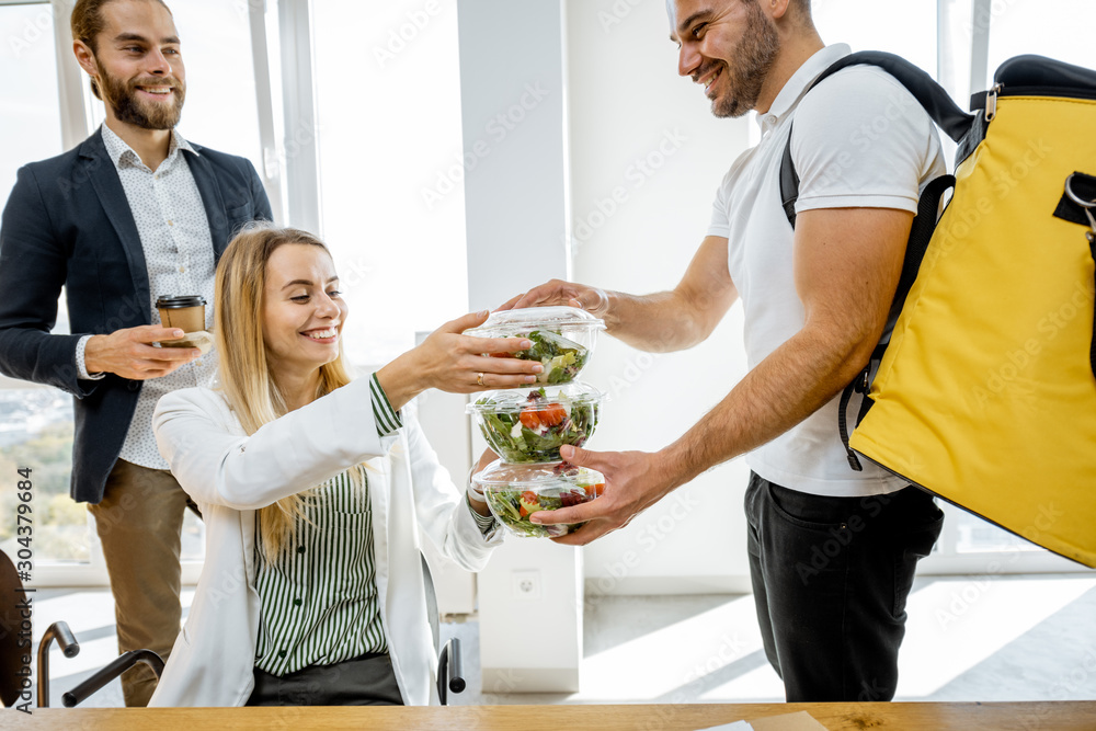 Courier delivering healthy business lunches with thermal bag for the office employees, giving them t