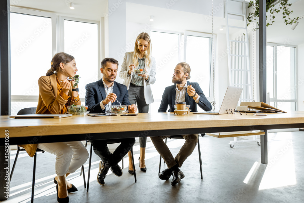 Group of a young office workers eating salads and drinking coffee at the modern office canteen. Conc