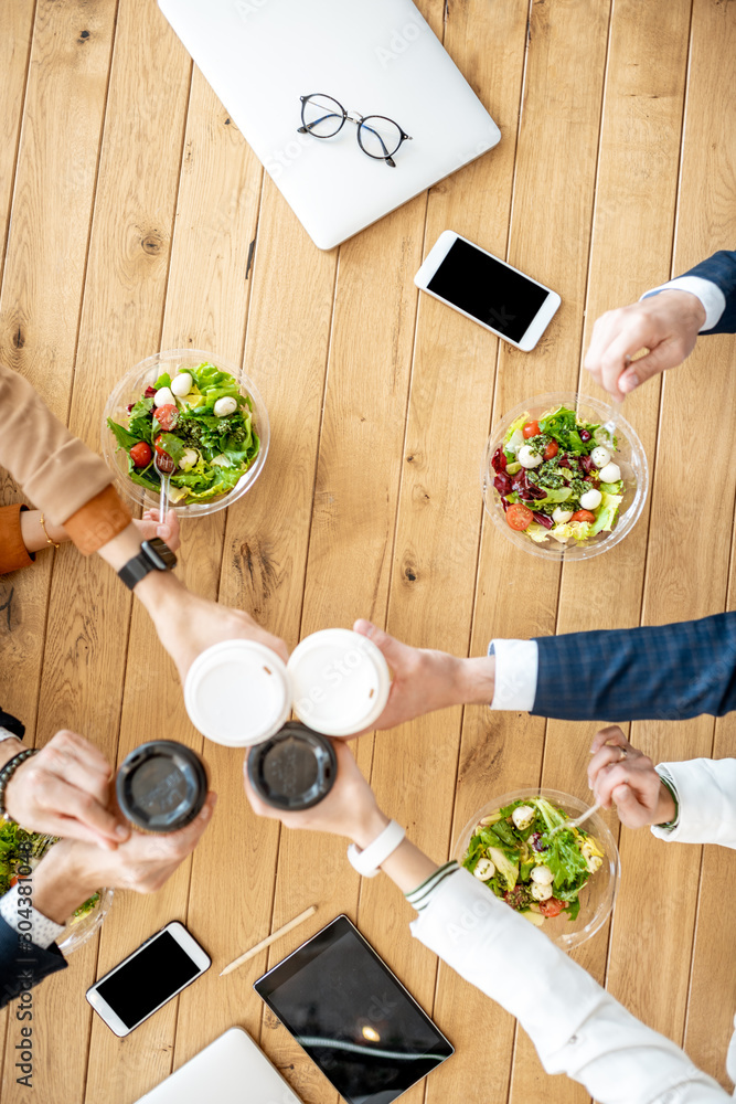 Office workers clinking coffee cups during a business lunch with healthy salads, view from above on 