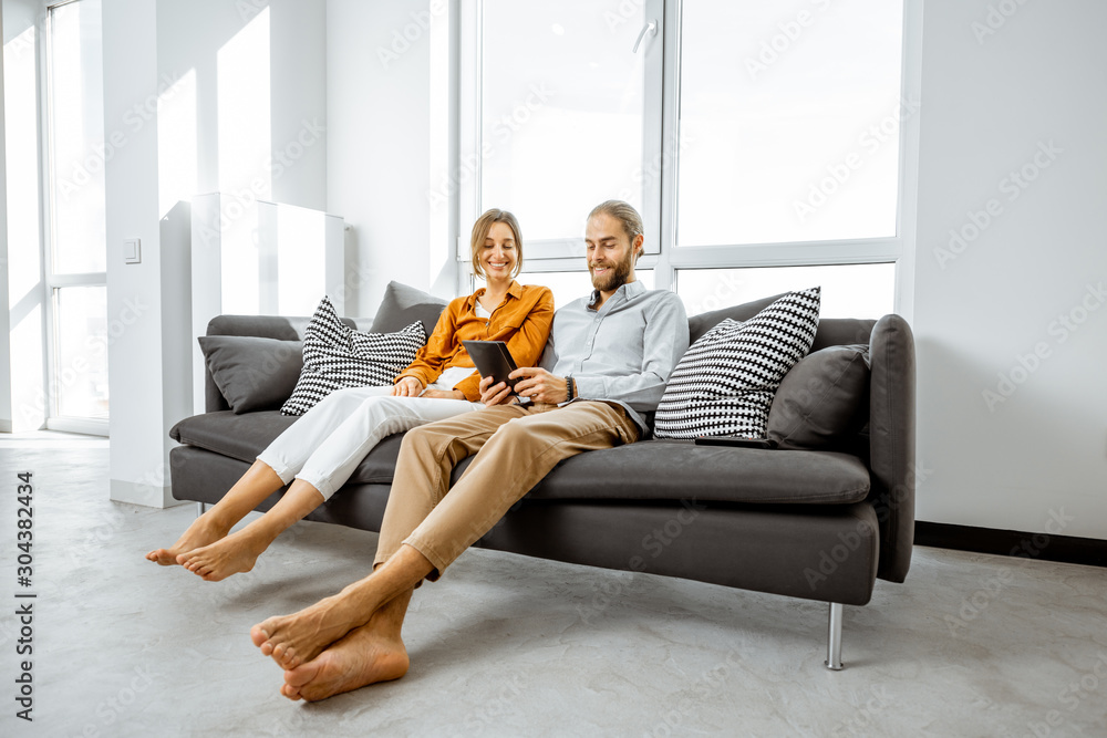 Happy young couple using digital tablet while sitting together on the couch in the bright living roo