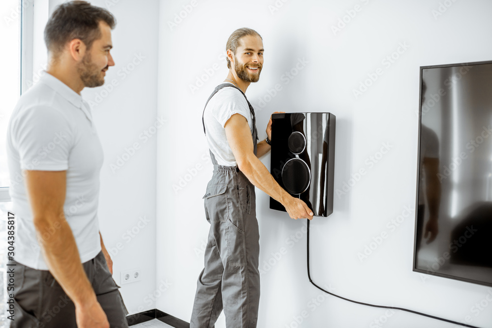 Two professional workmen in workwear installing luxury audio system in the white living room. Home a