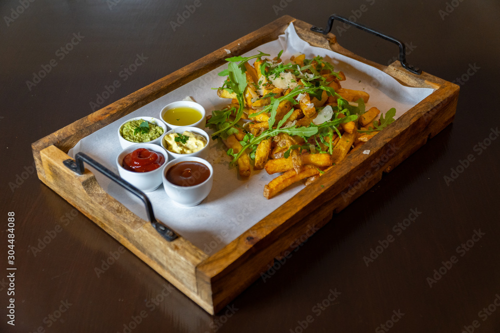 A wooden tray full of fresh fries with rocket salad, parmesan cheese and various dips