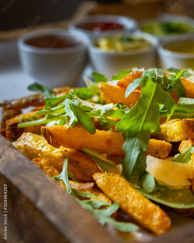 A wooden tray full of fresh fries with rocket salad, parmesan cheese and various dips