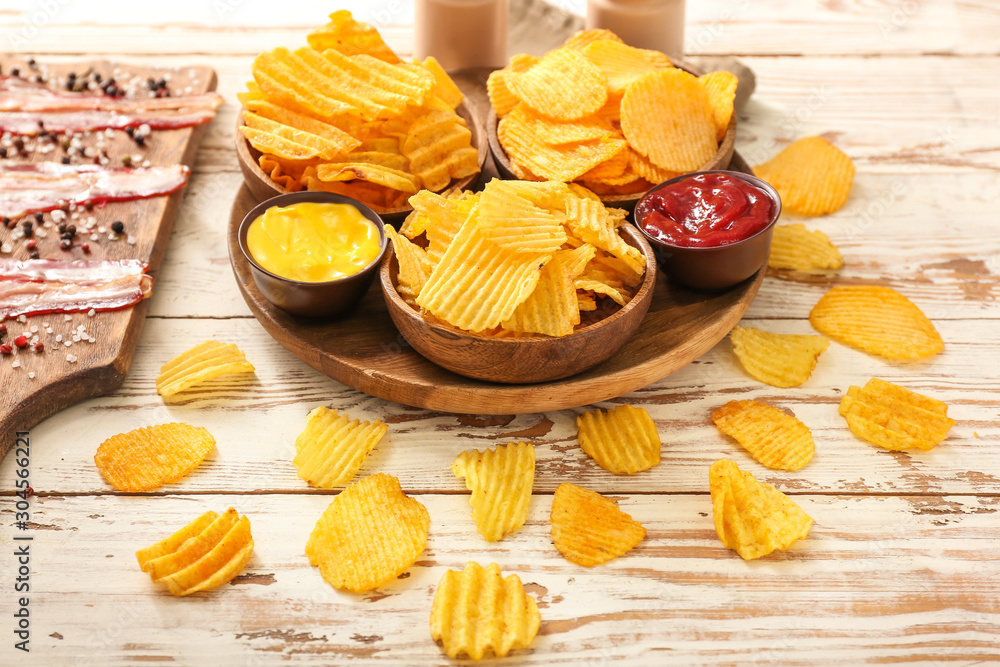 Tasty potato chips and bacon on light wooden background