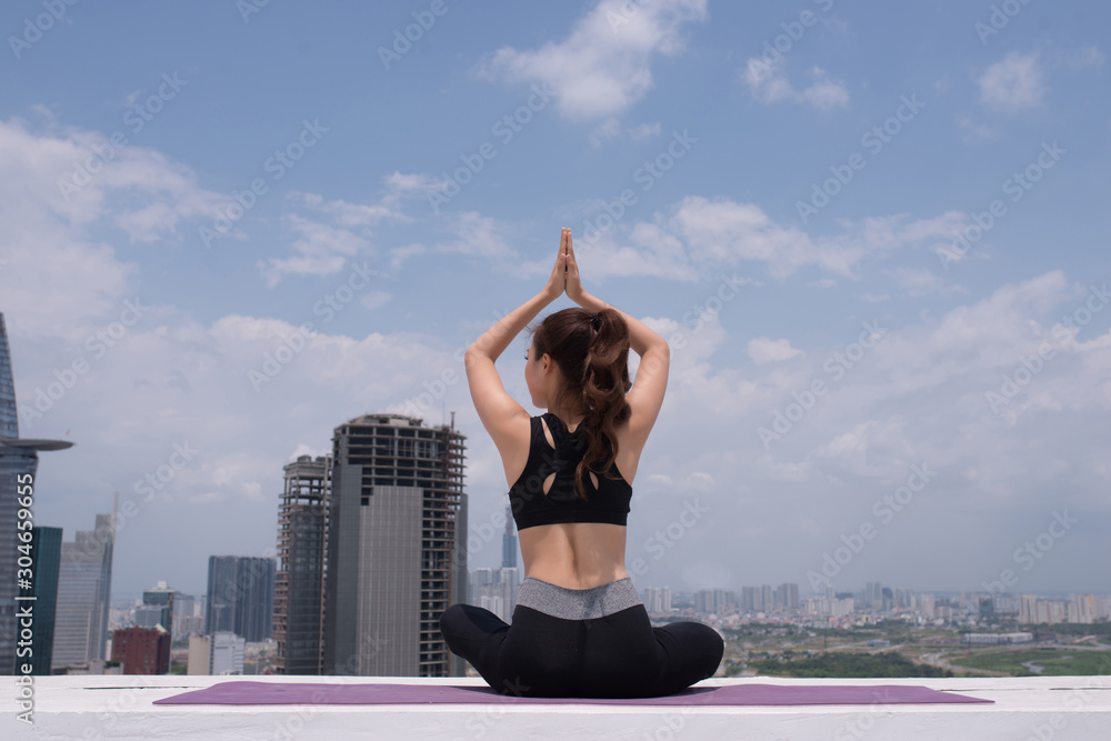 在屋顶上进行瑜伽训练时，身穿运动服的冷静年轻女运动员坐姿