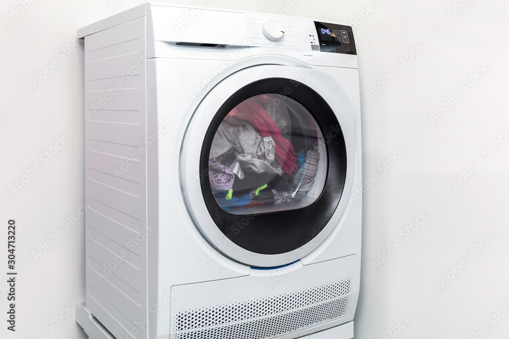 Electric dryer with clothes inside in the laundry room