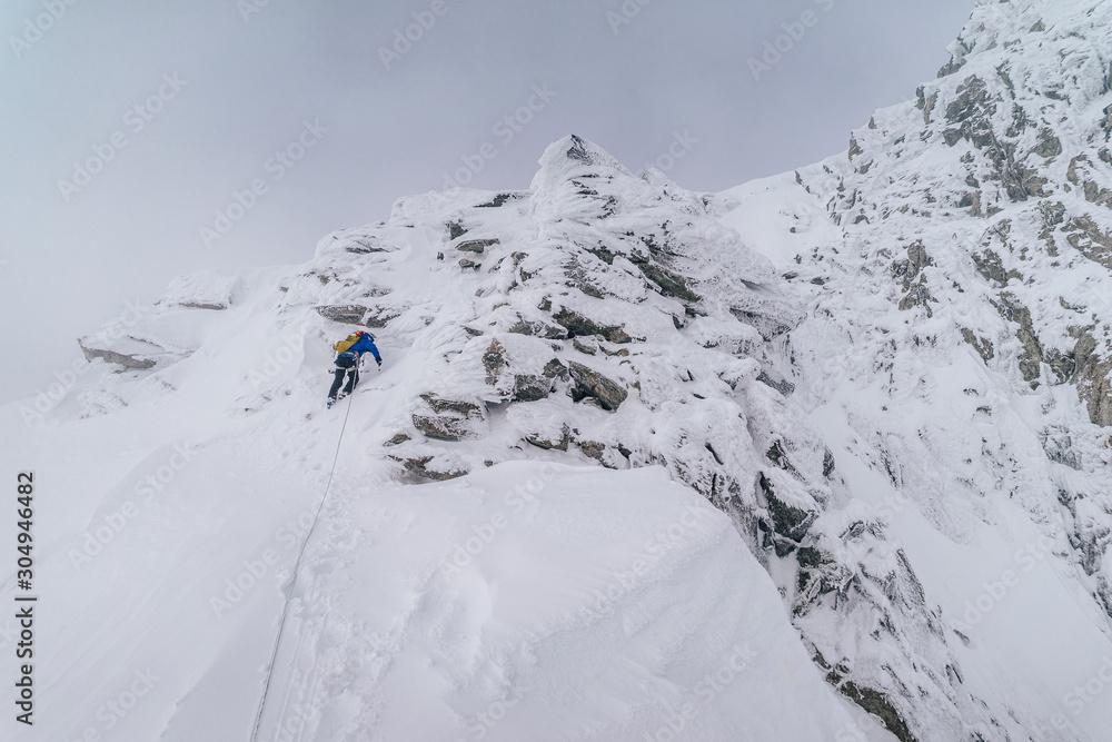 An alpinist climbing an alpine ridge in winter extreme conditions. Adventure ascent of alpine peak i