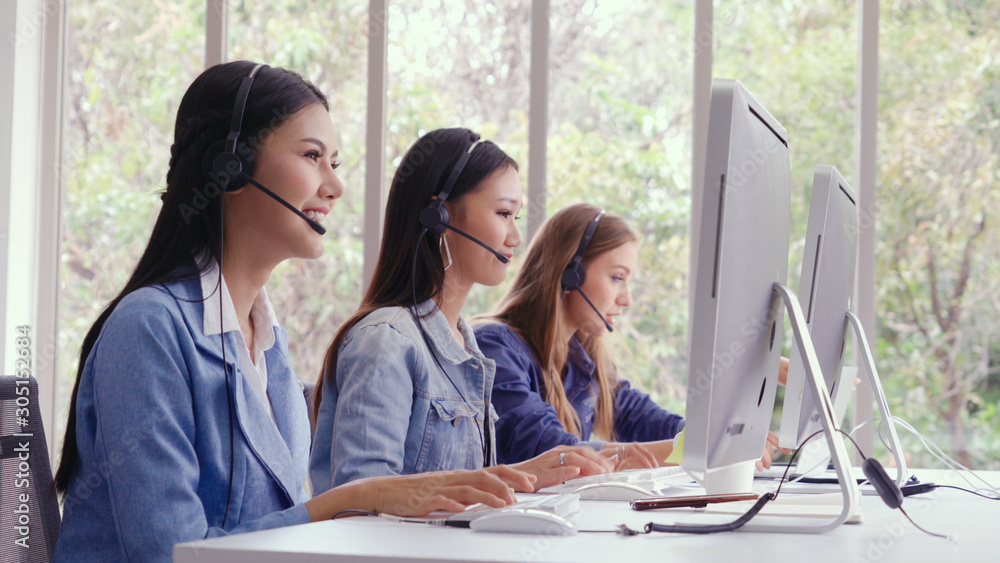 Customer support agent or call center with headset works on desktop computer while supporting the cu