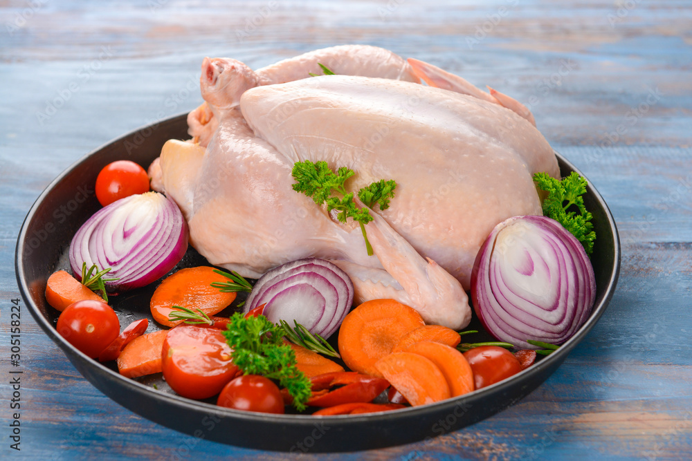 Frying pan with raw chicken and vegetables on wooden background