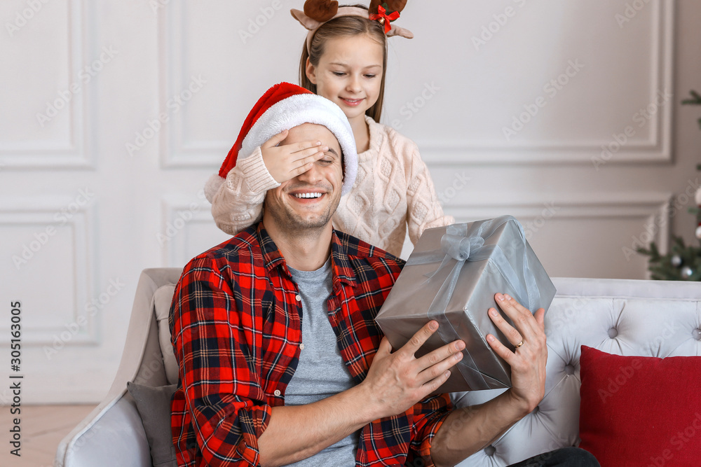 Little girl giving Christmas present to her father at home