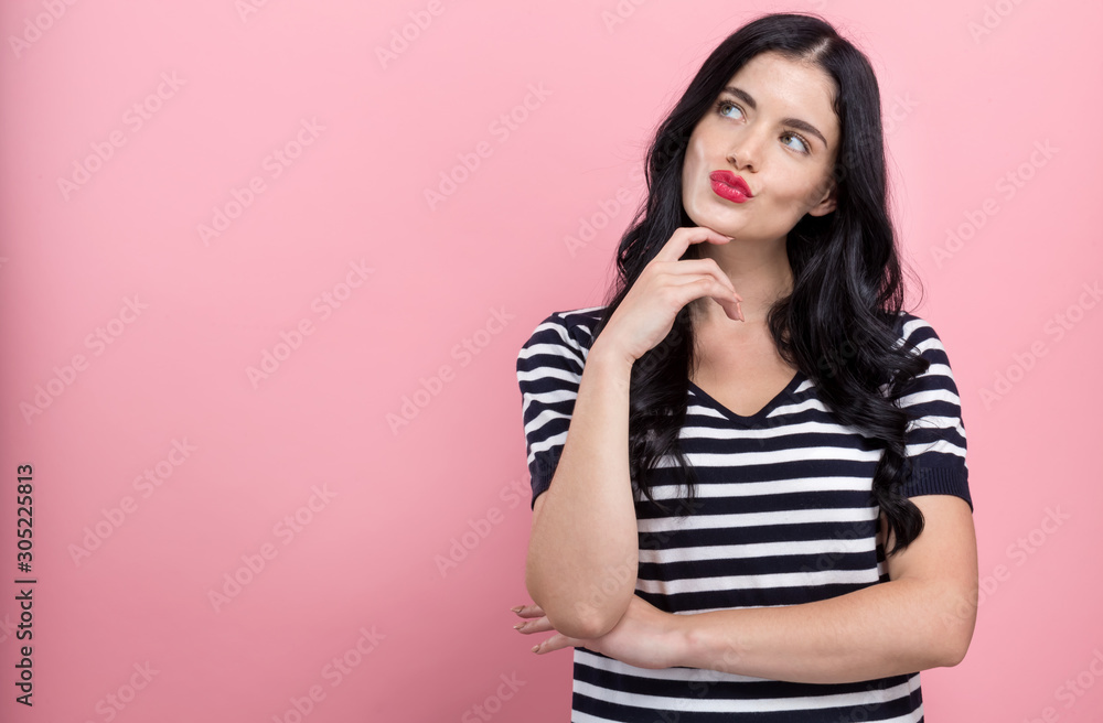 Young woman in a thoughtful pose on a pink background