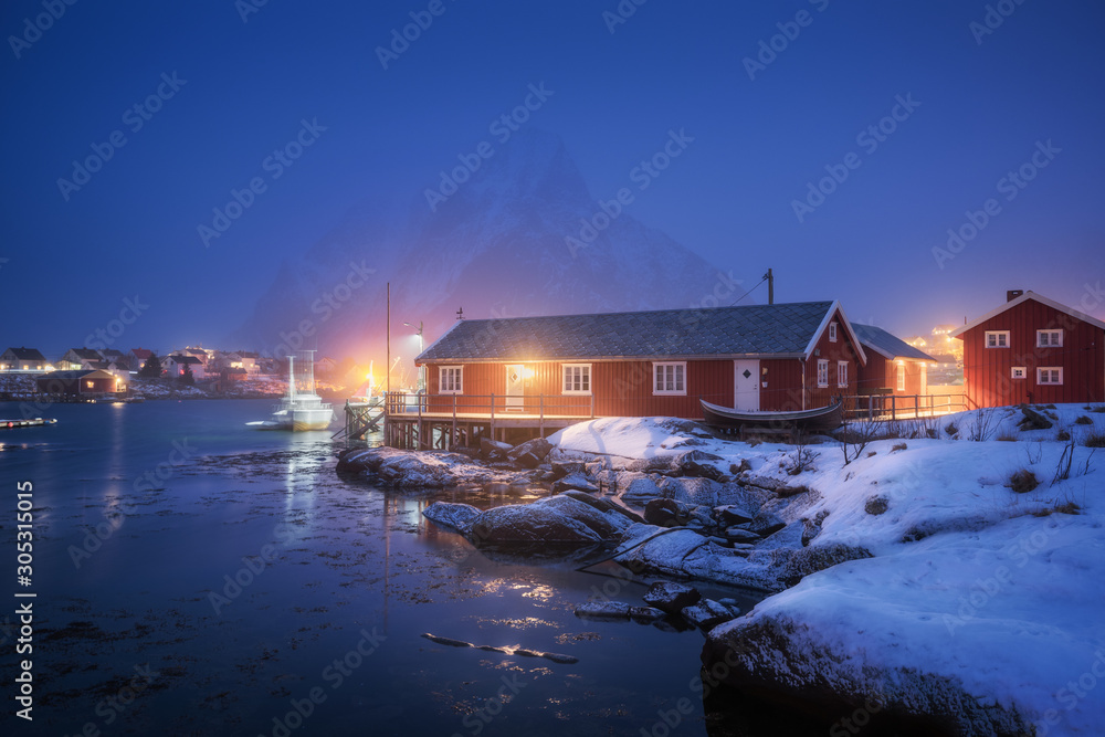 Beautiful norwegian Rorbu on sea cost and snowy mountain at night in winter. Lofoten islands, Norway