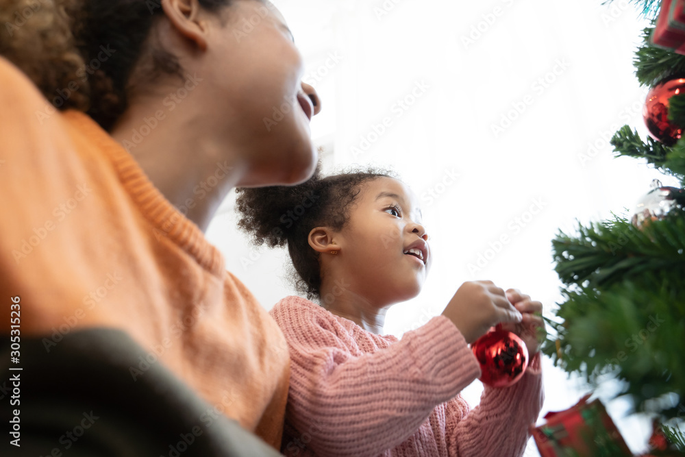 Mother and daughter african american girl decorating Christmas tree with ,arranging the christmas li