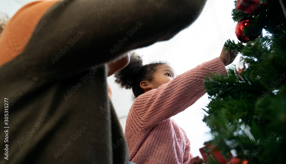 Mother and daughter african american girl decorating Christmas tree with ,arranging the christmas li