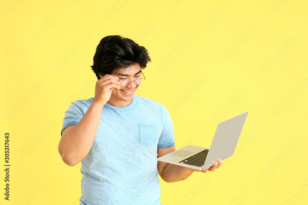 Male Asian programmer with laptop on color background