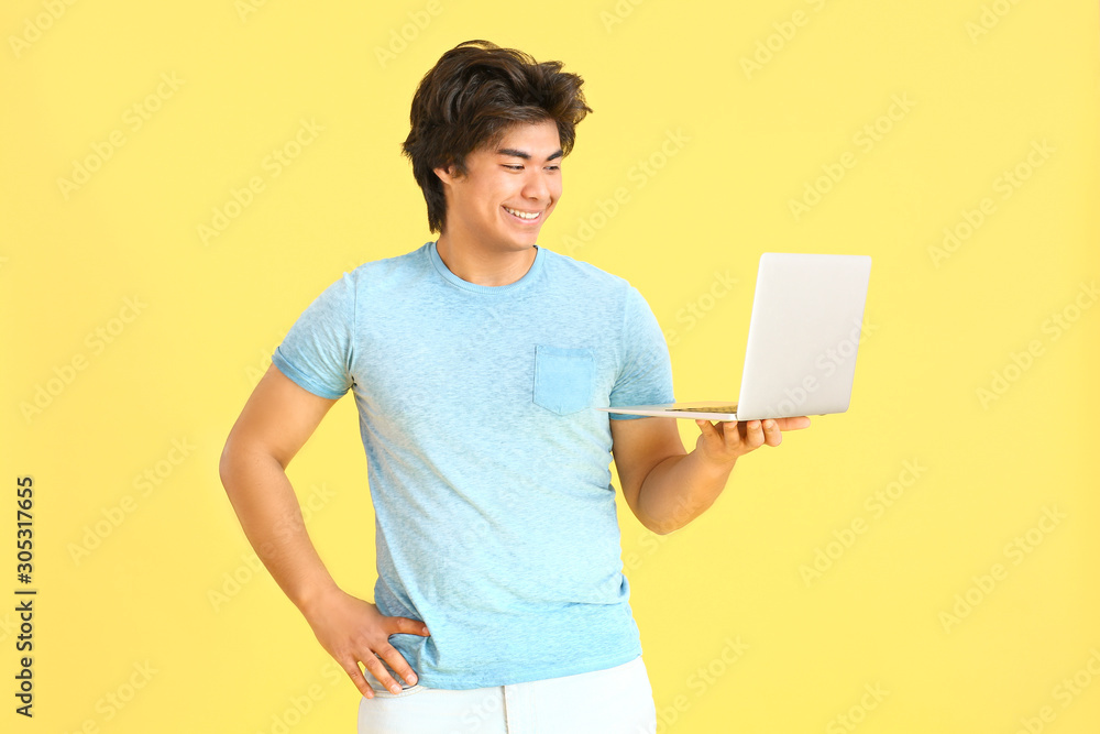 Male Asian programmer with laptop on color background