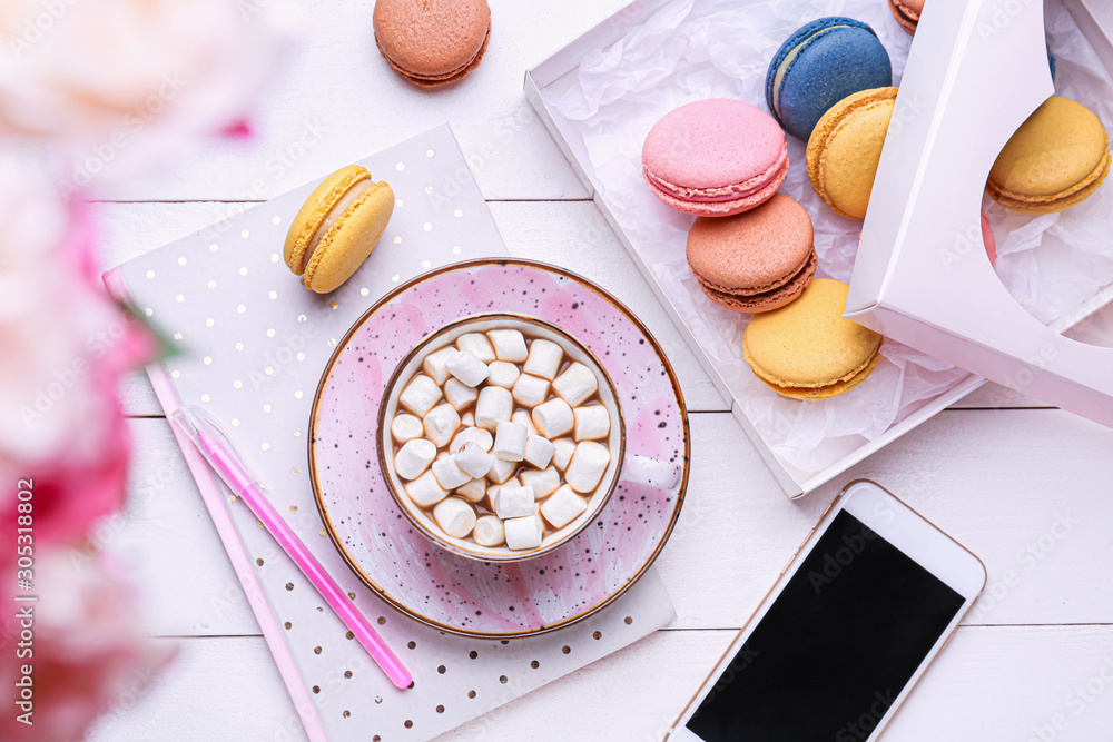 Cup of hot chocolate with tasty macarons and mobile phone on table