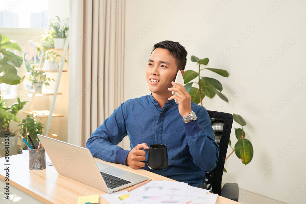 Businessman talking on the phone while drink coffee/tea at his working desk.