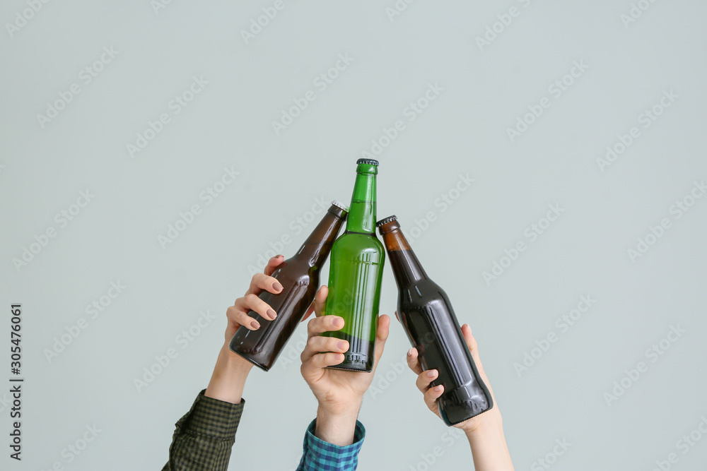 Hands clinking bottles of beer on grey background