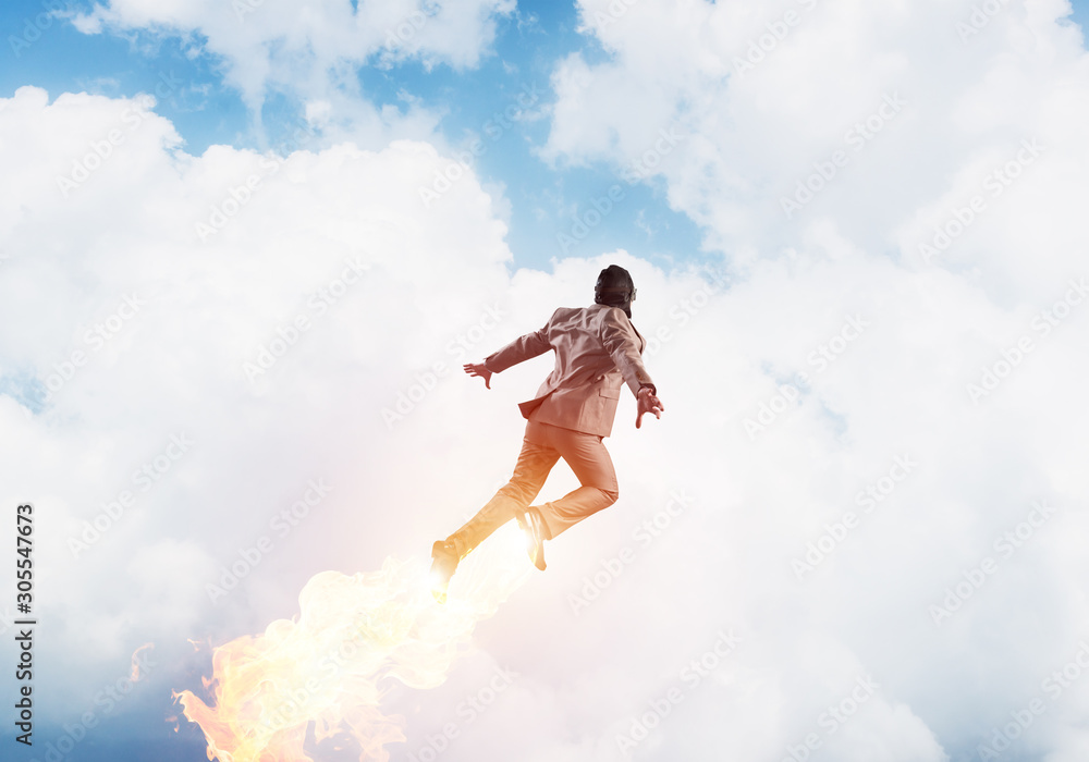 Businessman in suit and aviator hat flying in sky