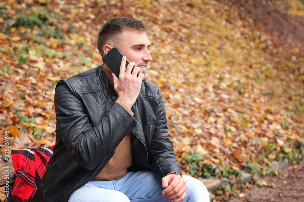 Handsome young man talking by mobile phone in autumn park