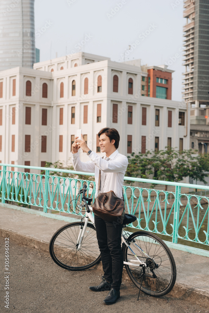 年轻人骑着自行车站在城市街道上用智能手机拍照