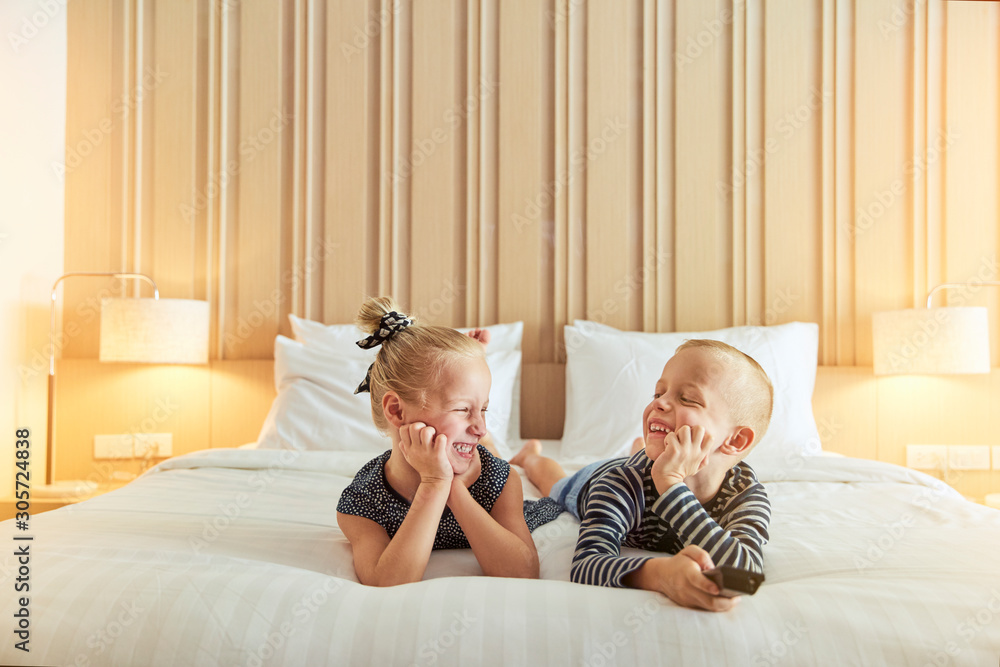 Laughing little brother and sister watching tv on a bed