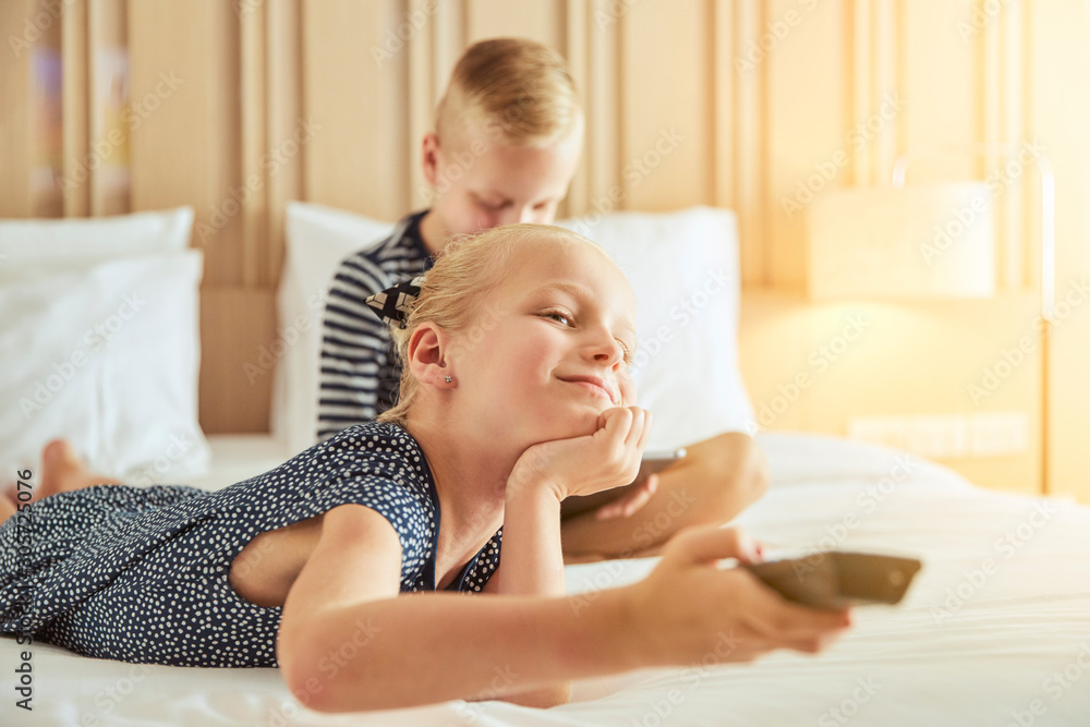 Little girl and her brother watching tv on a bed