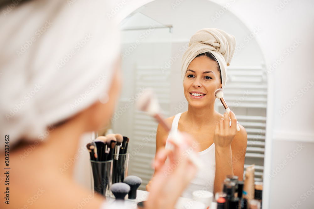 Young woman applying blush with make up brush in the bathroom.