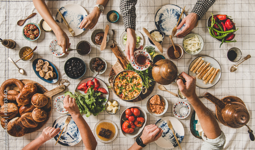 Flat-lay of family having Turkish breakfast with fresh pastries, vegetables, greens, spread, cheeses