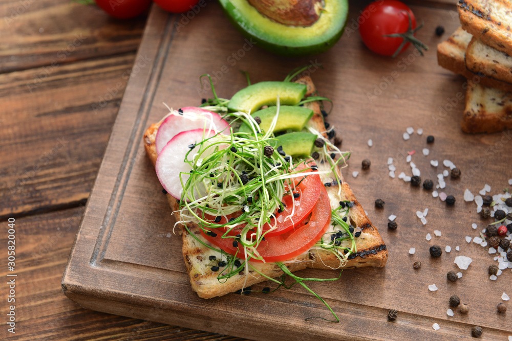 Tasty avocado sandwich and spices on wooden board, closeup