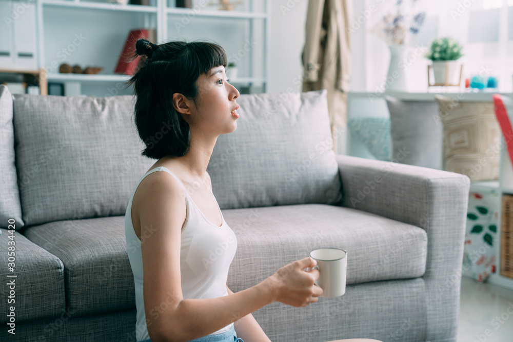 年轻可爱的亚洲日本女孩坐在现代客厅公寓里，手里拿着白色杯子。漂亮的wo