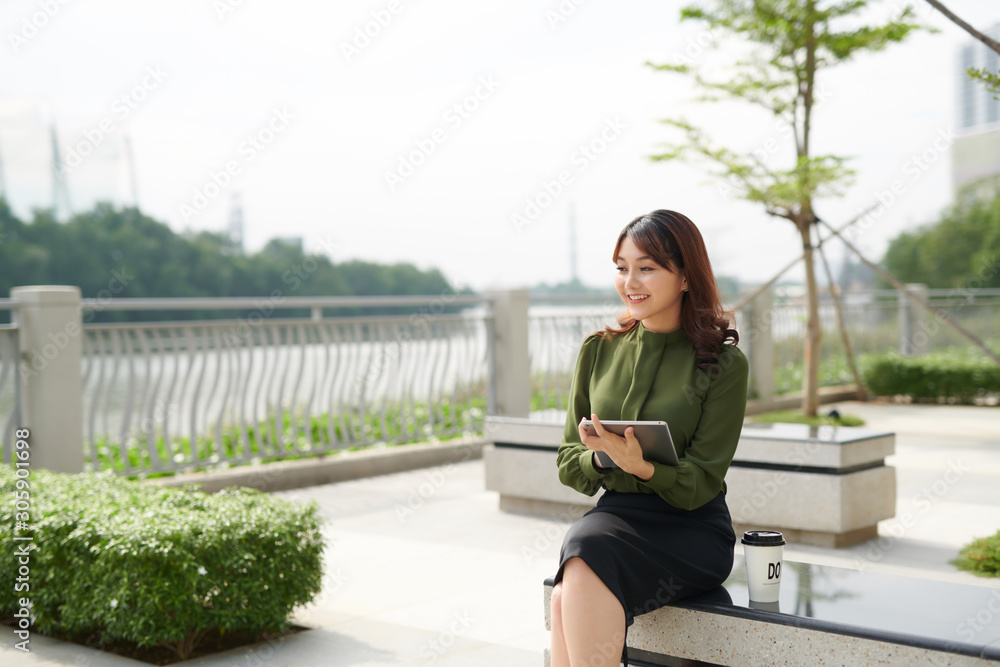 亚洲年轻女子在长椅公园上网玩平板电脑