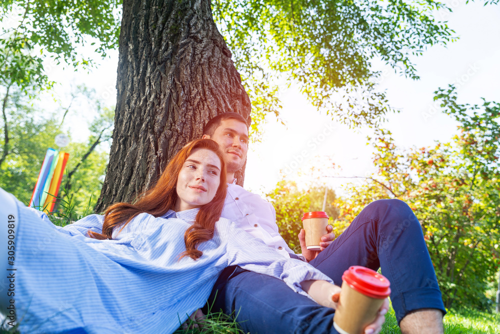 Young couple relaxing with coffee under tree