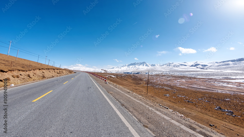 中国西北高原弯曲沥青路的中心视图，有秋天的牧场和雪山