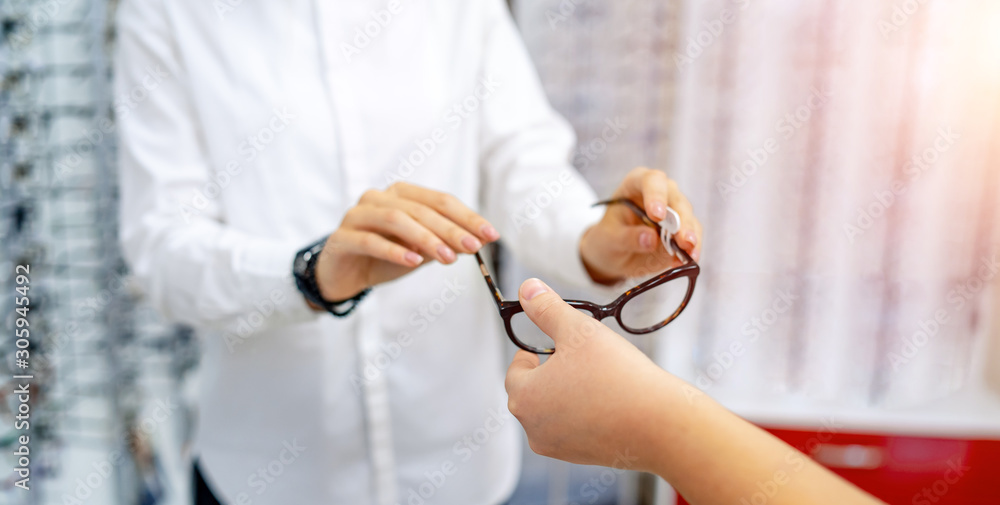 Cropped shot of a woman giving out glasses to the customer. Raw with spectacles in a background. Vis