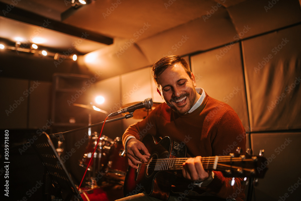 Portrait of a cheerful singing man with a guitar in the studio.