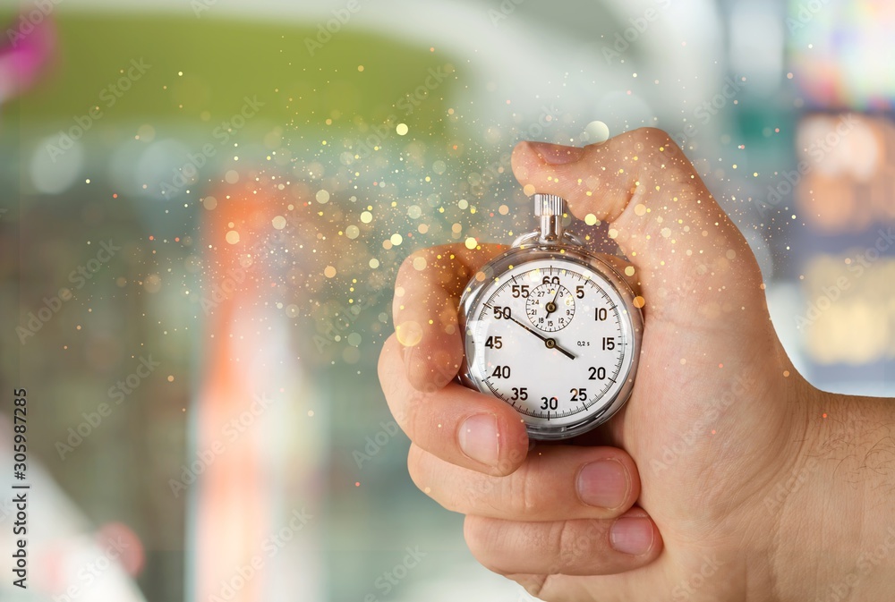 Stopwatch in human hand with flying shining lights on a colorful background